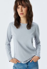 Lichtgrijze longsleeve shirt met een ronde hals, zachte textuur en een relaxte pasvorm. Gecombineerd met blauwe jeans met een casual ontwerp.