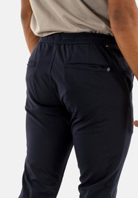 Pantalones jogger en color marino con cintura elástica, dos bolsillos traseros con cremallera y una tela suave y elástica. Presenta un detalle de marca mínimo.