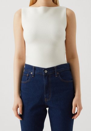 Geribd wit tanktop met ronde hals, gecombineerd met high waist donkerblauwe denim jeans met standaard zakken en contrasterend stiksel.