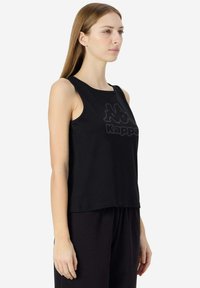 Canottiera nera senza maniche in cotone, caratterizzata da unlogo Kappa prominente sul davanti e una vestibilità comoda, abbinata a pantaloni scuri.