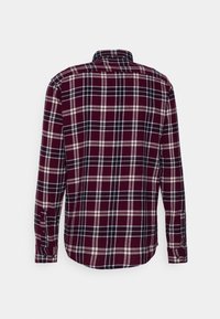 Camisa de cuadros en rojo y azul marino, con botones, cuello, mangas largas y dobladillo curvado. La tela tiene un acabado texturizado con costuras visibles.