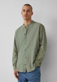 Lichtgroen overhemd met lange mouwen en een mandarinakraag, met knopen aan de voorkant en een losse pasvorm; gecombineerd met blauwe denim jeans.