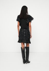 Fekete ruha texturált virágdíszítésekkel, fodros aljjal és fodros ujjakkal. Fekete, testhezálló térdcsizma párosítva hozzá.