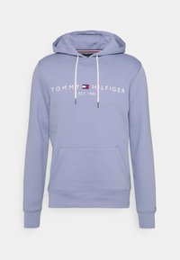 Felpa con cappuccio di un leggero colore viola, dotata di tasca anteriore a marsupio, lacci bianchi e logo "TOMMY HILFIGER EST. 1985" stampato sul petto.