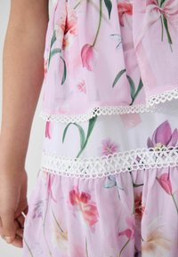 Rotes Blumenkleid aus leichtem Chiffon, mit mehreren Rüschen und weißer Spitze sowie verschiedenen Blumenmustern und Akzenten.