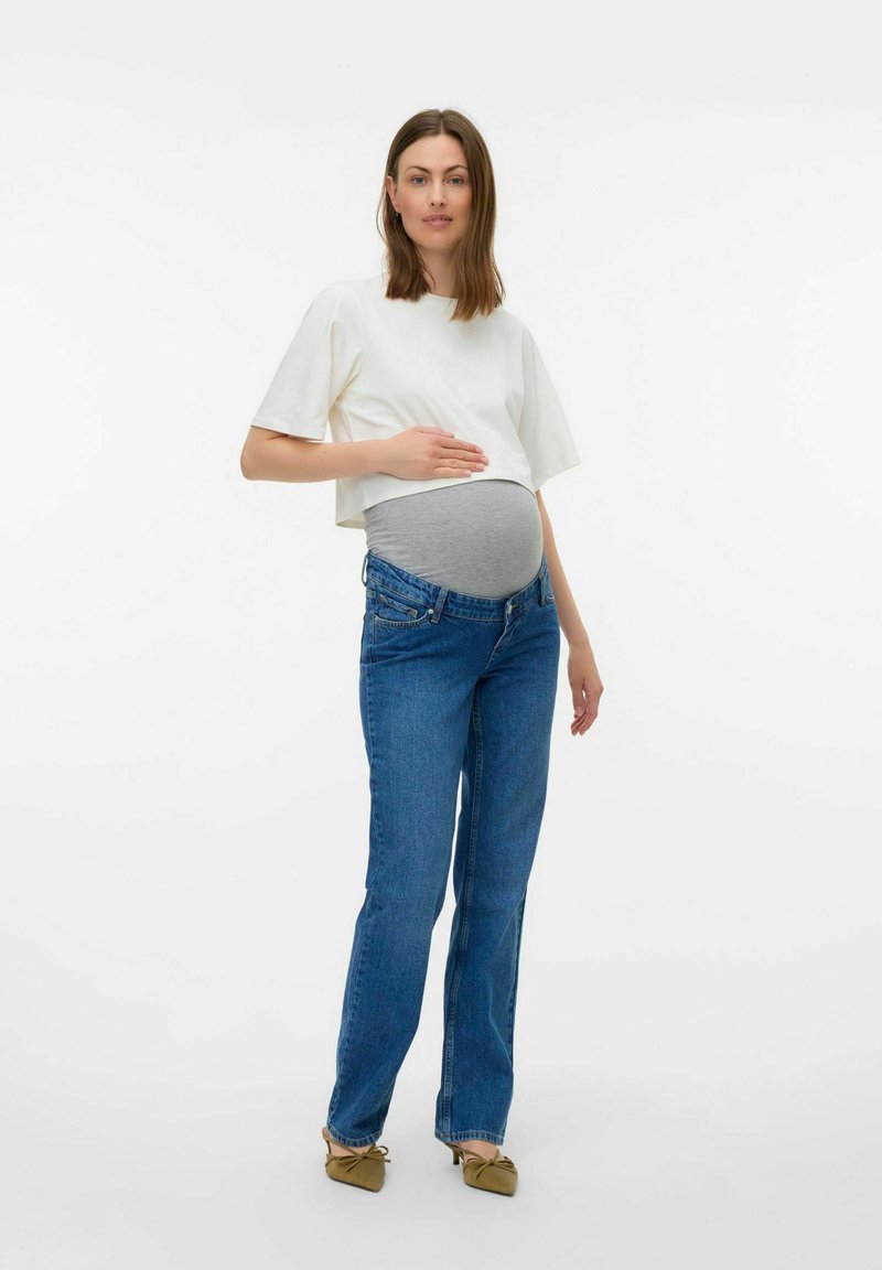 Maternitetna obleka, ki vključuje belo kratko majico, sivo raztegljivo ploščo in modre jeans hlače z ozkim krojem in rahlim zvončastim robom.