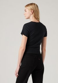 Tricou negru ajustat cu mâneci scurte și decolteu rotund, asociat cu blugi negri care au două buzunare la spate și detalii de cusătură subtile.