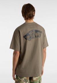 Khaki t-shirt made of cotton with a relaxed fit. Features a large black "VANS OFF THE WALL" graphic on the back.