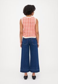 Haut en tricot sans manches à motifs rouge et blanc avec un design en vagues, associé à un jean en denim bleu à jambes larges avec un ourlet effiloché.