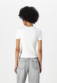 T-shirt bianco aderente a maniche corte con colletto rotondo, abbinato a jeans di denim grigi chiari, larghi, con tasche posteriori.