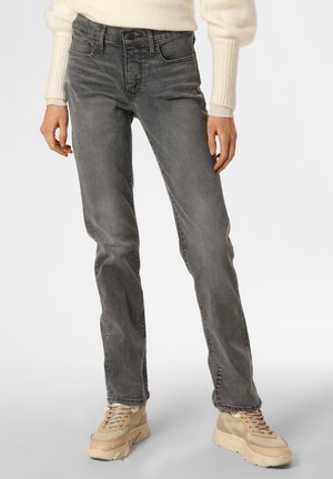 Personne portant un jean gris droit, des baskets beige épaisses et un pull crème à manches longues avec des poignets côtelés.