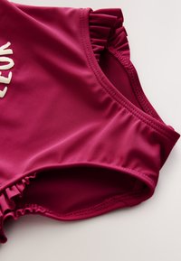 Fuchsia badpak met gerimpelde schouderdetails, met een gladde textuur en doorgestikte naden. De stof is lichtgewicht en rekbaar.