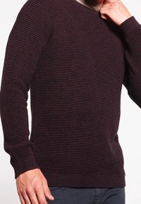 Stickad tröja i mörk burgund för färg med en texturerad yta, rundad halsringning och ribbade manschetter och fåll, med långa ärmar och en figursydd silhuett.