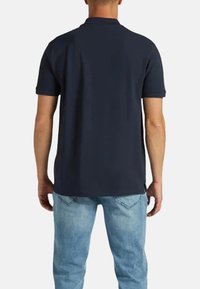 Polo blu navy con maniche corte e colletto, realizzato in tessuto morbido, con orlo dritto e spacco laterale nella parte inferiore.