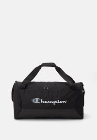 Bolsa de deporte negra hecha de un tejido resistente, con un compartimento principal con cremallera, asas para llevar y un logo destacado de Champion.