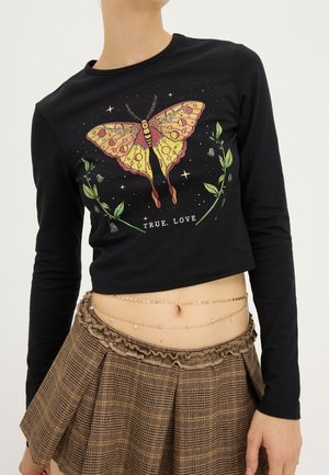 Zwart cropped top met lange mouwen met grote gele en roze mot, groene planten en de tekst "TRUE. LOVE", gecombineerd met een bruin ruitjesrok met plooien.