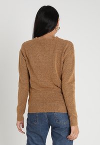 Maglione lavorato a maglia di color marrone chiaro con una finitura testurizzata, caratterizzato da un collo arrotondato e maniche lunghe, abbinato a jeans in denim blu.