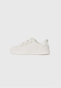 Hvide syntetiske sneakers med velcro-stropper, afrundet tå, diskret syning og en metallisk sølvaccent ved hælen. Glat tekstur.
