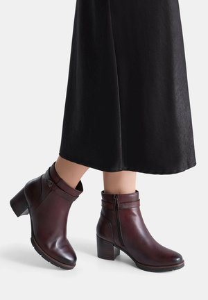 Bordo kožne gležnjače s okruglim vrhom, zatvaranjem na patentni zatvarač i debelom petom; glatka tekstura s kontrastnim prošivenim detaljima.