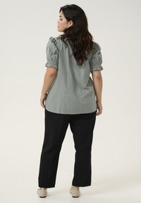 Lichtgroene blouse met pofmouwen, met geplooide details. Gecombineerd met zwarte broek en lichte schoenen. Eenvoudig en casual ontwerp.