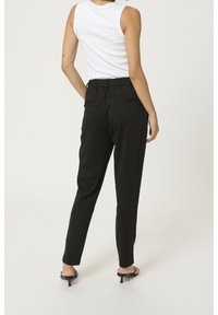 Pantalons noirs fuselés avec une ceinture froncée, dotés de deux poches arrière et d'une finition lisse, associés à un débardeur blanc.