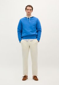 Blauwe sweatshirt met capuchon en trekkers, gecombineerd met lichtkleurige linnen broek en bruine leren schoenen. Eenvoudig ontwerp en ontspannen pasvorm.