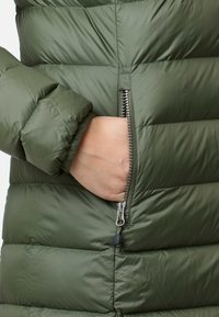 Grön vadderad jacka med en slät yta, utrustad med en ficka med dragkedja och elastiska ärmslut för ökad värme och komfort.