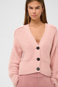 Růžová pletená cardigan s výstřihem do V, žebrovanou strukturou a třemi černými knoflíky vpředu. Má široké rukávy a zkrácený střih.