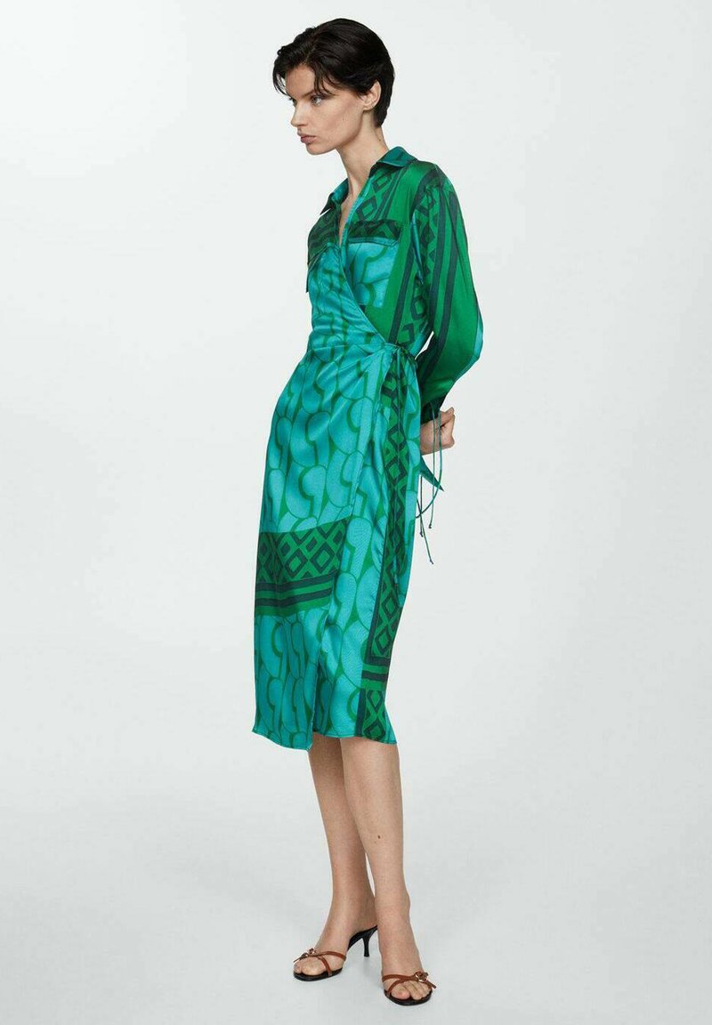 Rochie verde, cu mâneci lungi, cu modele geometrice și un detaliu cu funda în talie. Material neted, ușor, cu o finisare lucioasă.