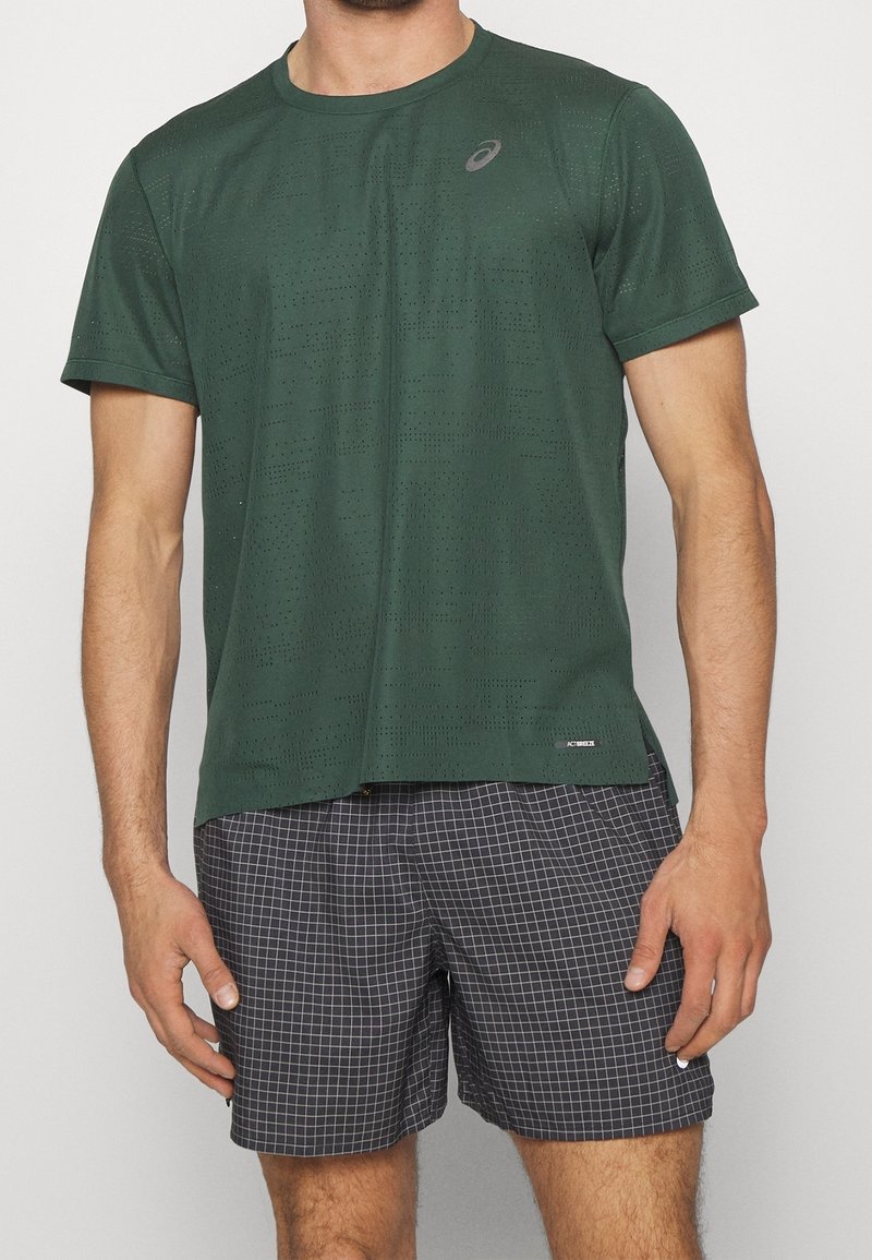 Dark green short-sleeve athletic shirt with a crew neck, featuring perforated texture and logo, paired with black grid-patterned shorts.