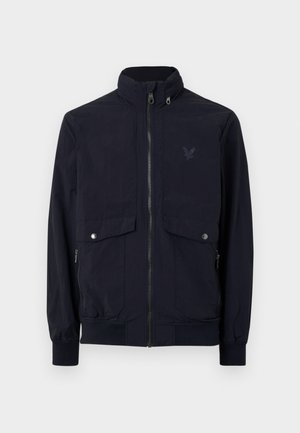 Marine blauwe ritsjack gemaakt van lichtgewicht stof met een hoge kraag, twee voorzakken en geribbelde manchetten. Voorzien van een subtiel logo op de borst.