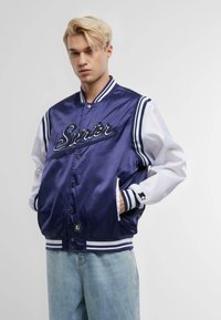Navy satin varsity jacket with white sleeves, embroidered "Starter" logo, ribbed collar and cuffs, button closure, and side pockets.