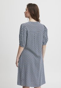 Šaty s krátkým rukávem s geometrickým modro-bílým vzorem. Vyrobené z lehké tkaniny, s uvolněnou siluetou a jemnými detaily na zadní straně.