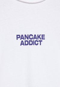 Witte stof met vetgedrukte paarse tekst in het midden, met de tekst "PANCAKE ADDICT" in hoofdletters.