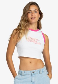Top corto blanco con ribetes rosas en el cuello y en las mangas. Presenta un texto elevado en rosa que dice "Roxy Surf Club". Combinado con pantalones cortos de tiro alto en azul claro.