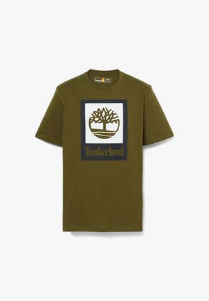 Oliwkowa koszulka z krótkim rękawem z białym kwadratem w czarnej ramce, z stylizowanym logo drzewa i napisem „Timberland” poniżej.