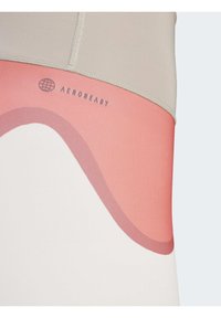 Koszulka sportowa z miękką beżową górą, z różowym i białym zakrzywionym wzorem. Zawiera szare logo "AEROREADY". Gładka struktura, dopasowany krój.