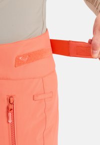 Koraalroze sportbroeken met een gladde textuur, voorzien van een klittenbandsluiting, een voorzak met rits en stiksel details aan de zijkanten.