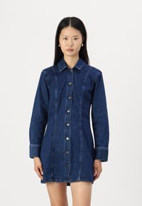 Denim obleka v temno modri barvi z dolgimi rokavi, gumbastim zapenjanjem in ovratnikom. Ima kontrastne šive in ravno krojnino.