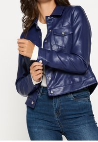 Giacca in ecopelle blu navy con colletto strutturato, chiusura a bottoni a pressione e due tasche frontali. Presenta un design leggermente accorciato.