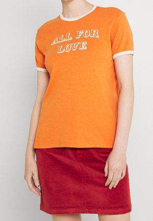 Pomarańczowa koszulka z krótkim rękawem z białymi wykończeniami oraz napisem "WSZYSTKO DLA MIŁOŚCI" w zakrzywionej czcionce. Materiał wydaje się miękki i lekki.