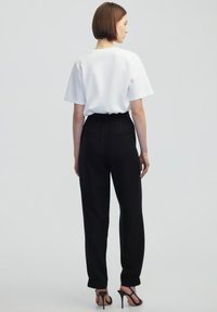 Witte korte mouwen shirt gecombineerd met hoge zwarte broek met een elastische tailleband en gathered manchetten, gezien vanaf de achterkant.