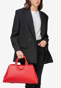 Rød lædertaske med en struktureret form, gyldne hardware-detaljer og dobbelte håndtag, parret med en sort blazer og hvid top.