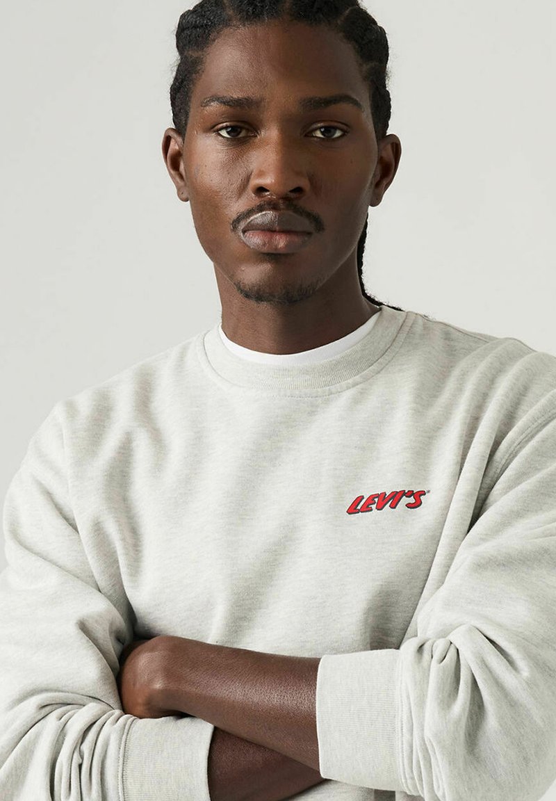 Sweat-shirt gris chiné avec poignets côtelés, encolure ronde et logo rouge "LEVI'S" sur la poitrine. Texture douce avec une coupe décontractée.