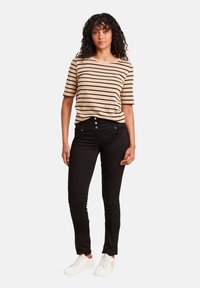 T-shirt beige à rayures avec des manches courtes, jeans slim-fit noirs et baskets blanches. Le t-shirt a un col rond et une coupe décontractée.