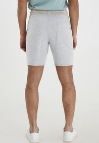 Grå bomullsblandingsshorts med en slitt kant, elastisk midje og en enkelt baklomme, sammen med hvite joggesko.