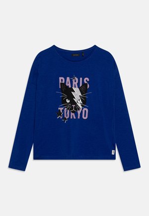 Langermige blauwe T-shirt met een grafiek van een zwarte kat, roze tekst met "PARIS TOKYO" en zilveren accenten voor extra detail.