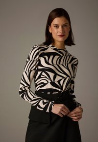 Long-sleeve top in beige and black with a leaf pattern, made of lightweight fabric. The sleeves have a gathered detail at the cuffs.