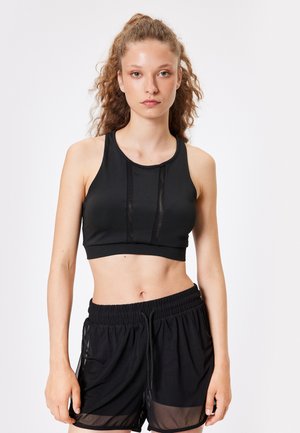 Sort sports crop top lavet af strækbart stof, med gennemsigtige paneler, parret med løse sorte shorts med mesh detaljer.