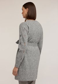 Szara dzianinowa sukienka swetrowa z paskiem w talii i wycięciami na rękawach. Miękka tekstura i średniej długości krój.